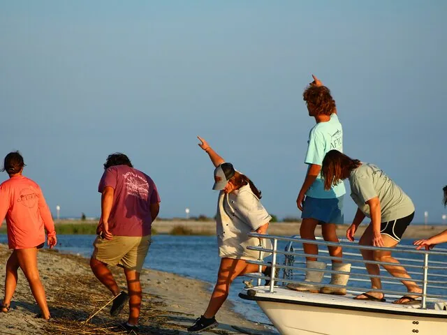 Un groupe de personnes monte à bord d'un bateau depuis un rivage sablonneux, pointant du doigt quelque chose.