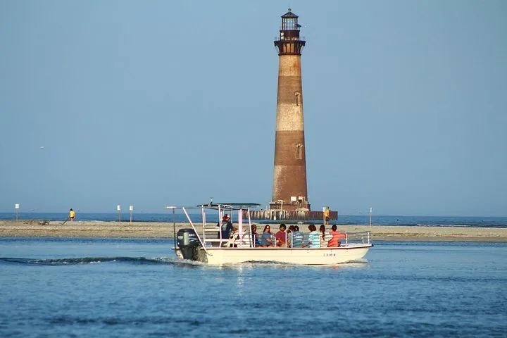 Un bateau rempli de passagers s'approche du phare de Morris Island dans des eaux calmes.