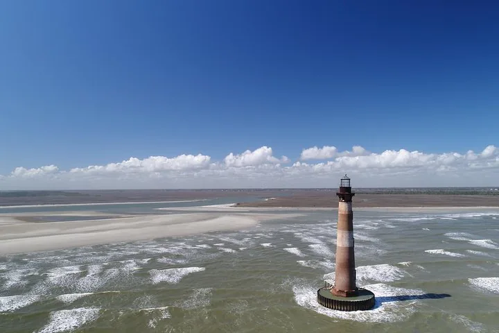Aerial view of Morris Island Lighthouse standing in the water near a sandy shore.